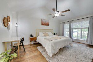 Modern guest bedroom at Destination Pine Walk in Spring TX featuring a queen bed, wood floors, natural light, and workspace — located 5 miles from the ExxonMobil Houston Campus.