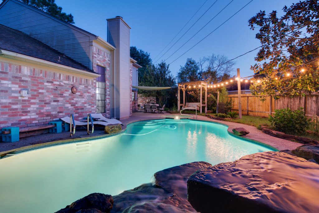 Nightime pool scene with waterfall in foreground and hanging lights across the edge in Spring Texas