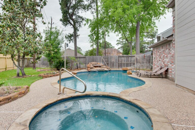 Private backyard with an in-ground pool and hot tub, rock waterfall feature, surrounded by lush trees in a Spring, Texas luxury home.