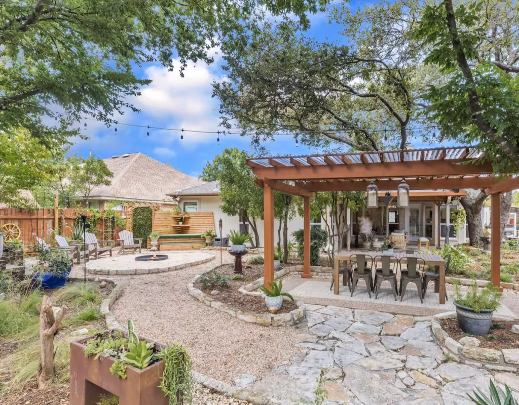 Outdoor garden oasis at The Garden House in Cedar Park, Texas featuring a pergola dining area, fire pit, and stone walkway.