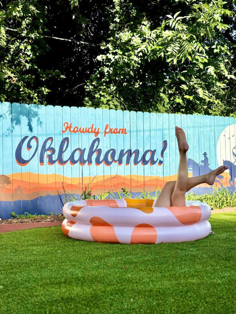 Howdy from Oklahoma mural at The Cowboy Retreat vacation rental in Oklahoma City — backyard view with inflatable pool and Western-style fence art