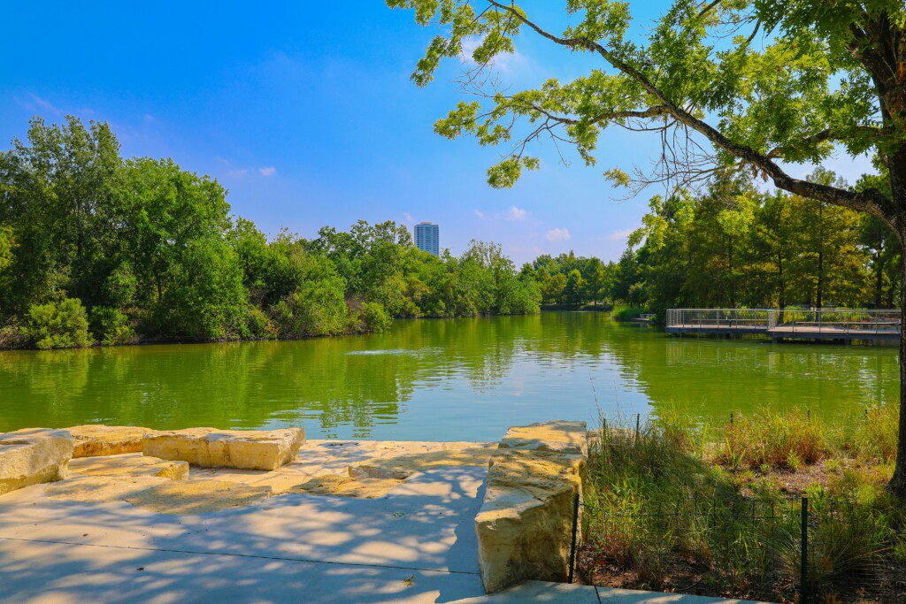 Hermann Park Houston green lake with stone seating area surrounded by lush trees and natural vegetation