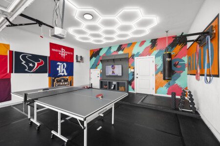 Full garage game room with ping pong table, Houston sports flags, and honeycomb LED lights at The Landing Pad Houston vacation rental near NRG Stadium