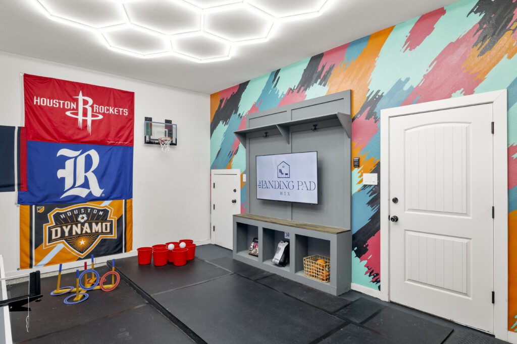 Garage game room with Houston sports flags, ring toss, and beer pong at The Landing Pad Houston vacation rental near NRG Stadium