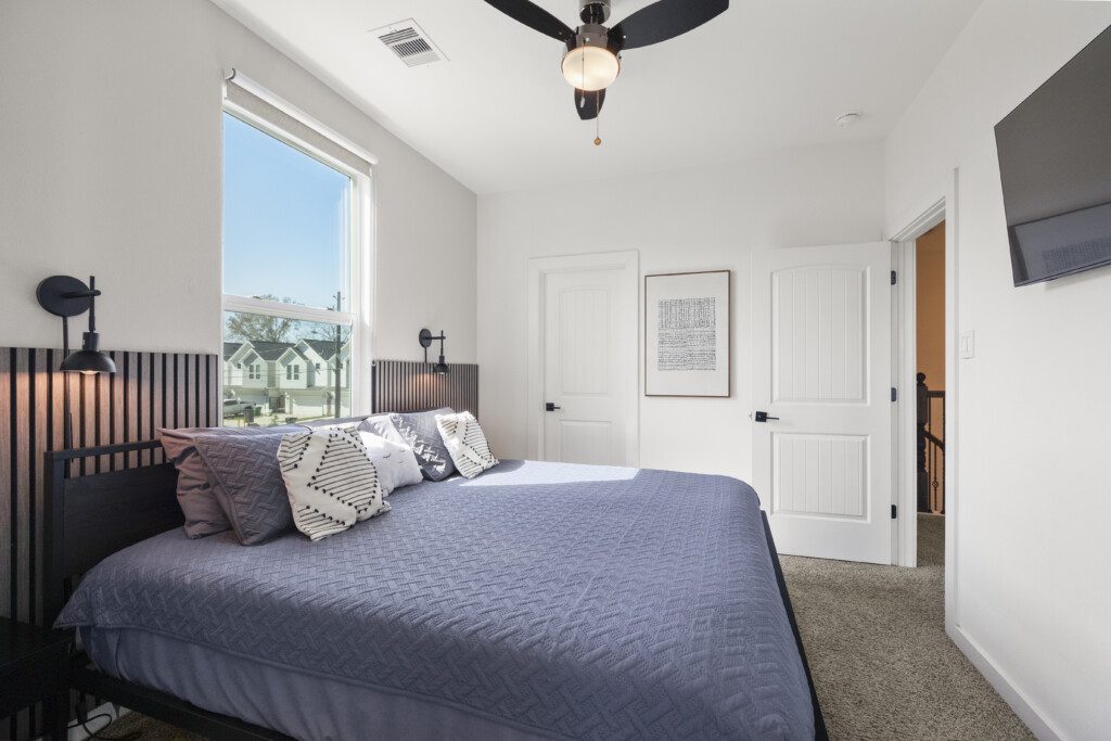 Guest bedroom with black slat headboard, Smart TV, and large window at The Landing Pad Houston vacation rental near NRG Stadium