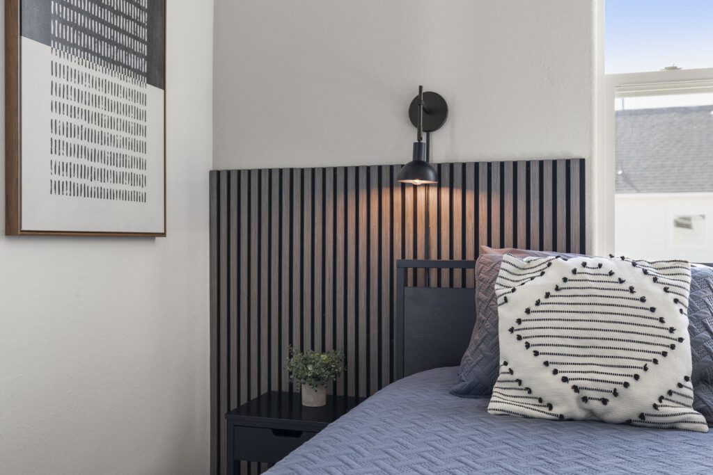 Guest bedroom detail with black slat headboard, wall sconce, and textured pillow at The Landing Pad Houston vacation rental near NRG Stadium